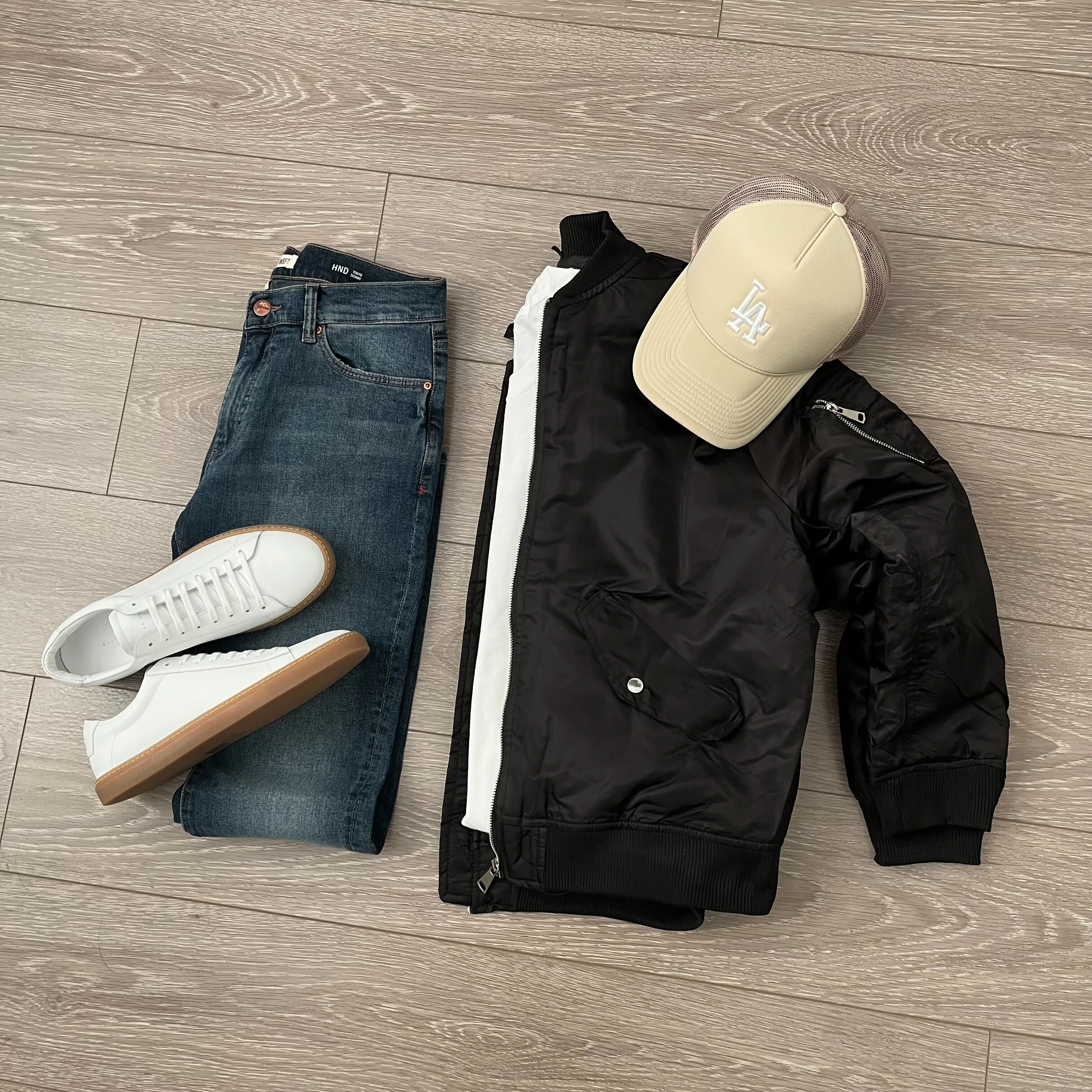 layout of a black bomber, tan hat, jeans, and white shoes
