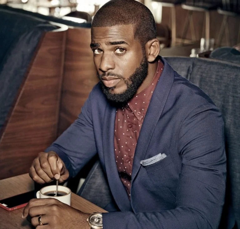 Chris Paul sitting in a blue suit and a red button up
